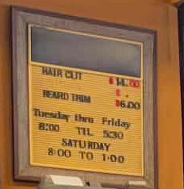 The letter board inside the shop listing haircut $14.00, beard trim $6.00, Tuesday through Friday 8:00 til 5:30, Saturday 8:00 to 1:00.