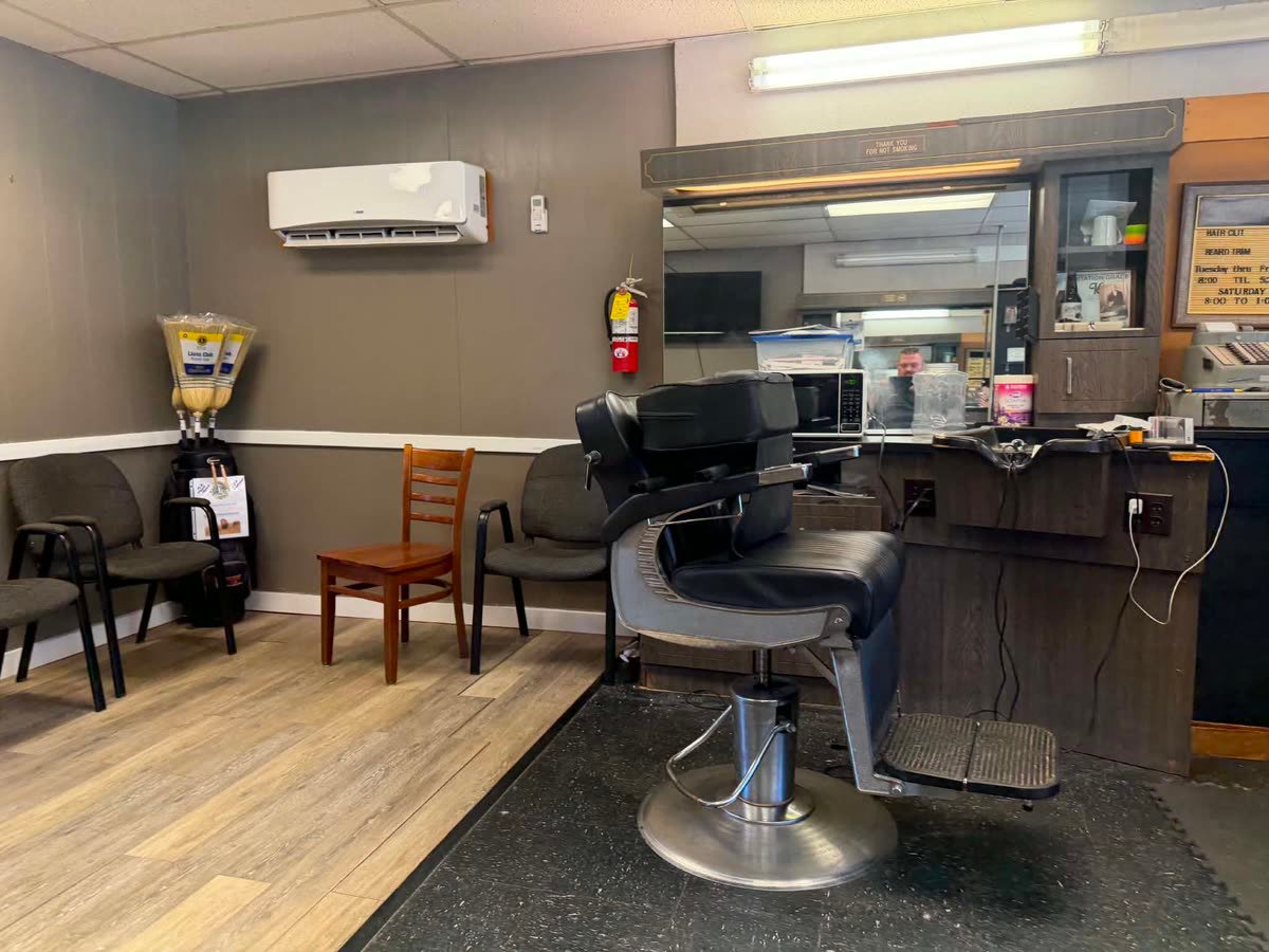 An empty pedestal barber chair beside the workstation and mirror.