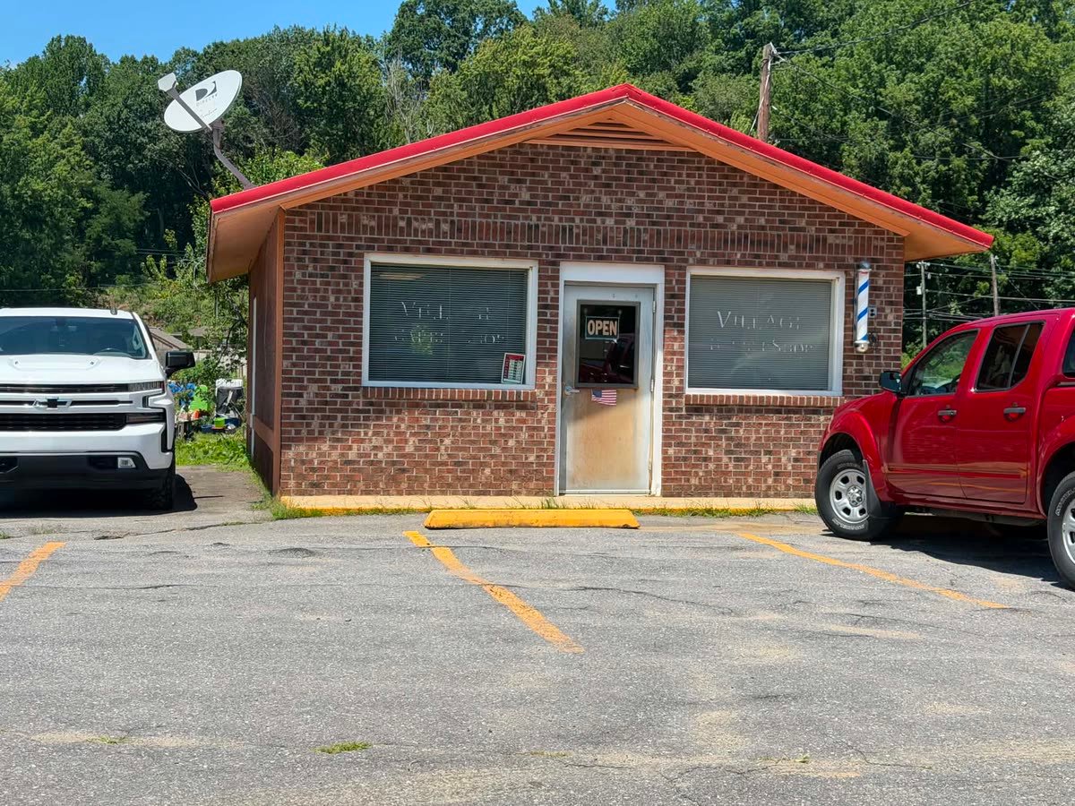 The brick barbershop with a red metal roof and a barber pole beside the door.